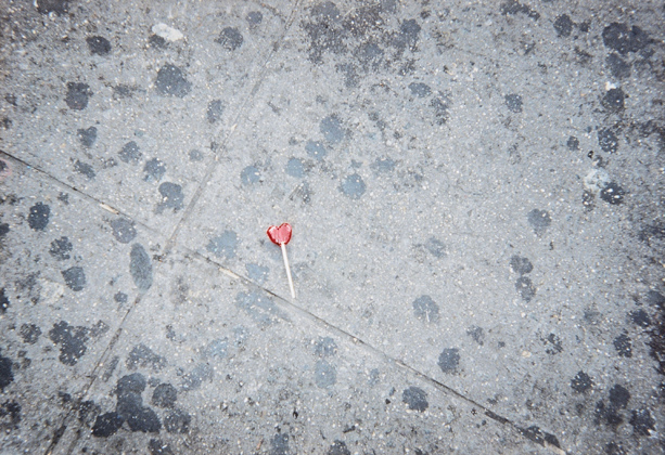 Sweetheart, 2002, On the soiled sidewalk, a single heart-shaped lollipop. Photo by Tony Feher
